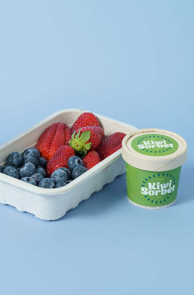 Container of strawberries and blueberries next to a cup of Kiwi Sorbet on a mid blue background from CM Props & Backdrops 