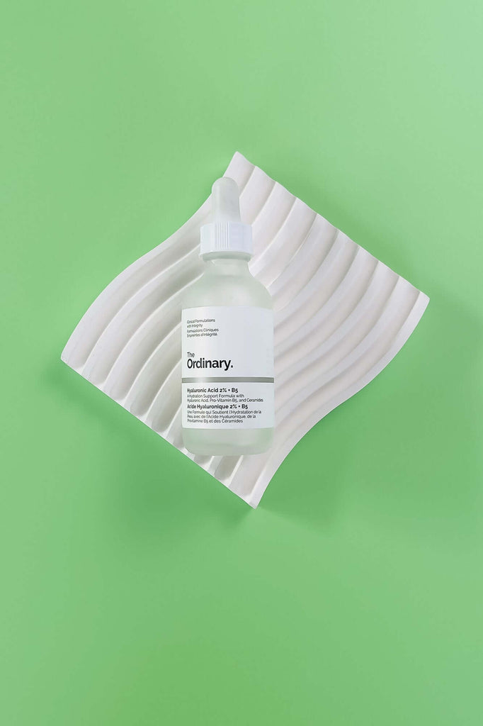 Skincare bottle with a white label on a textured white square against a green background