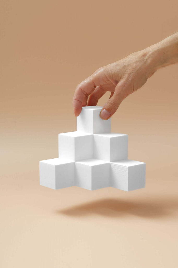 Hand holding white geometric blocks against a warm beige background, showcasing creativity and design elements.